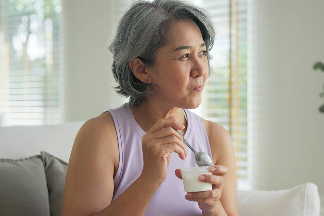A middle-aged woman at home eating a cup of yogurt.